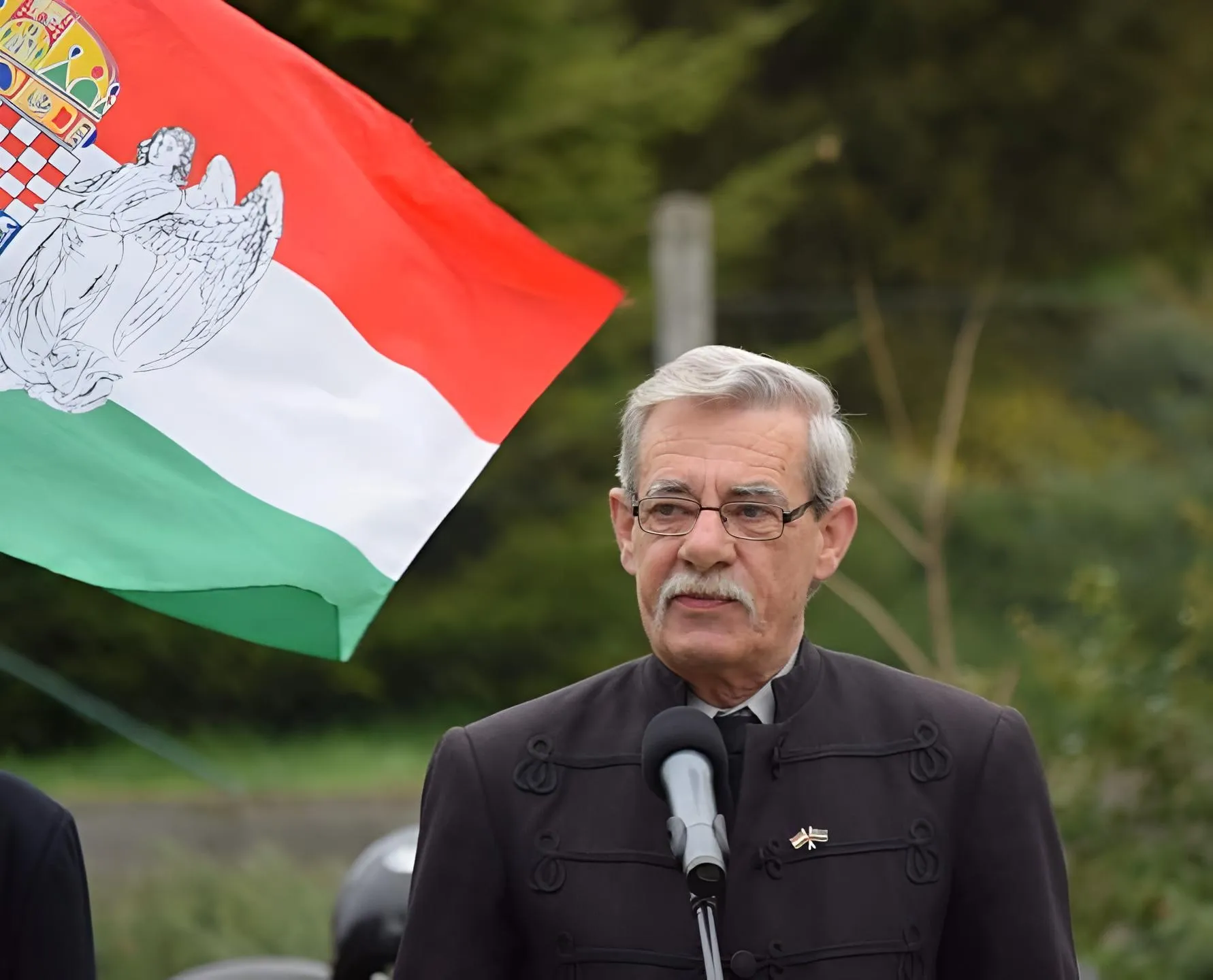 Bartha József vorbind la microfon, cu steagul maghiar în spatele lui.